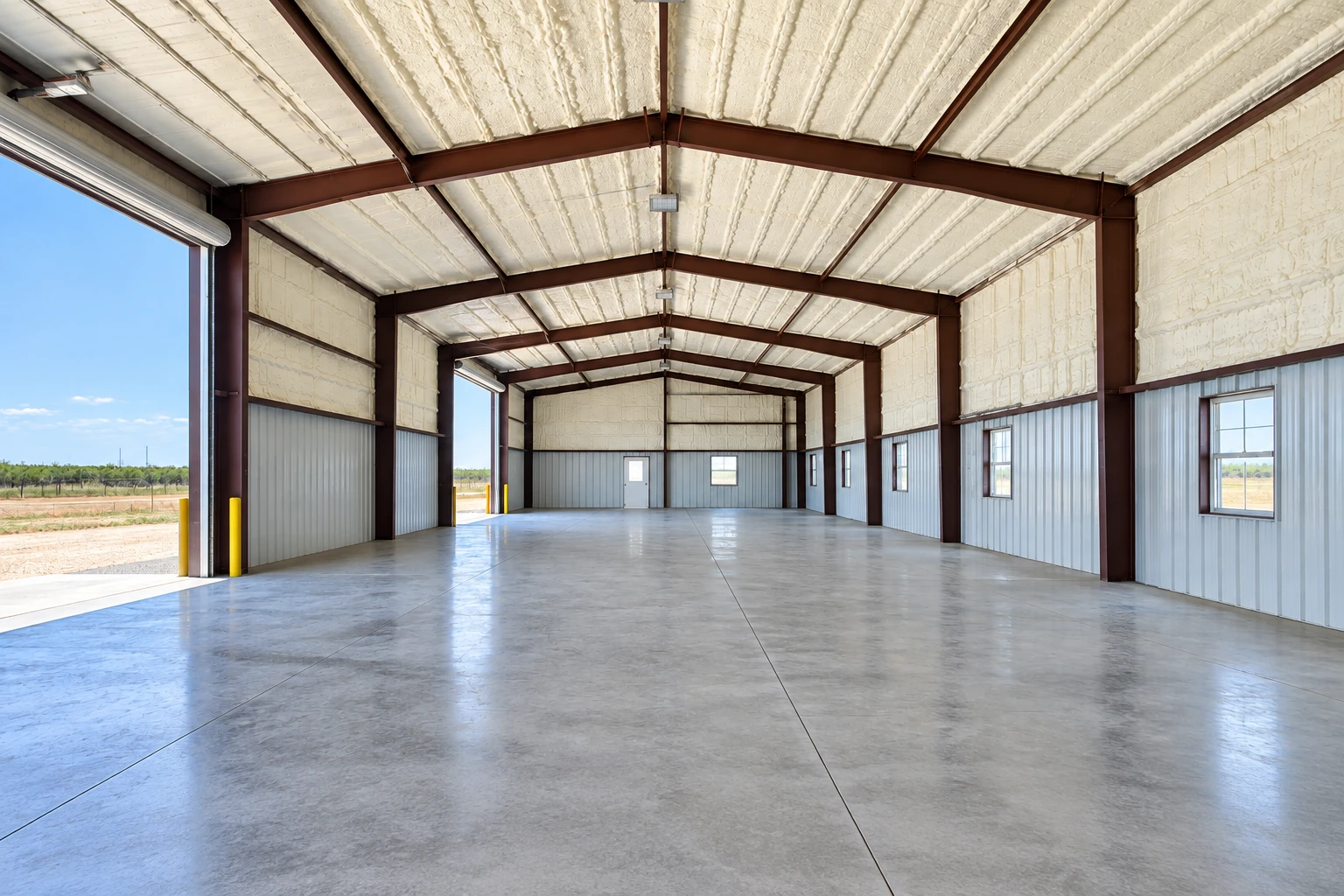 A large metal-frame commercial building has pale spray foam insulation across its roof and upper walls.
