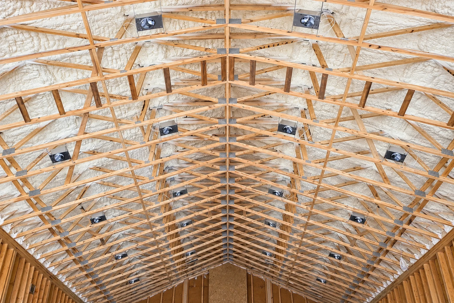 White spray foam coats the underside of a large timber roof, filling spaces between exposed trusses.