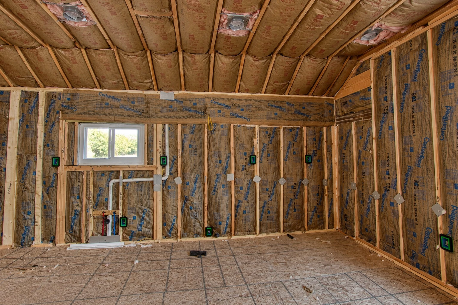 Unfinished room with fiberglass batts fitted between wall studs and ceiling joists, plus a window and exposed wiring.